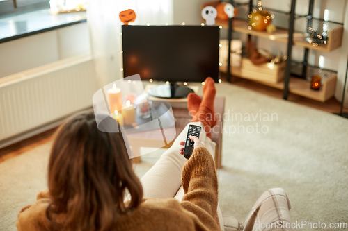 Image of young woman watching tv at home on halloween