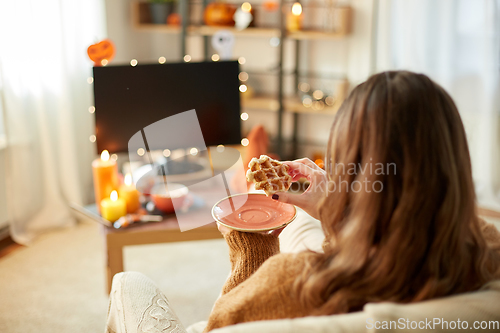 Image of woman watching tv and eating waffle on halloween