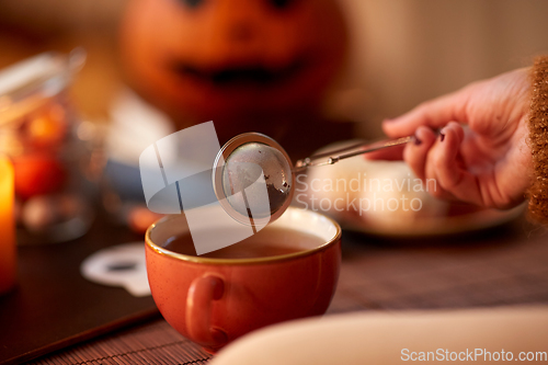 Image of woman's hand with tea infuser and mug on halloween