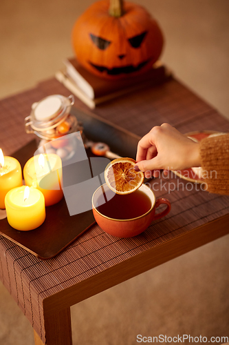 Image of hand adding dry orange to cup of tea on halloween