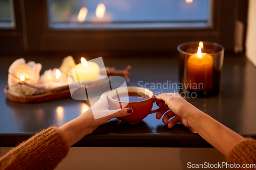 Image of hands with cup of tea on window sill in autumn