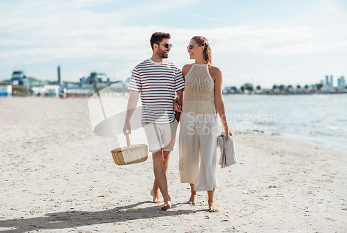 Image of happy couple with picnic basket walking on beach