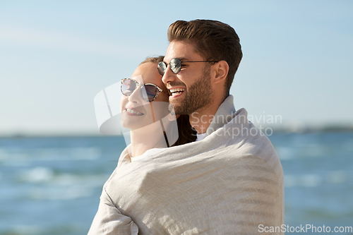 Image of happy couple covered with blanket hugging on beach