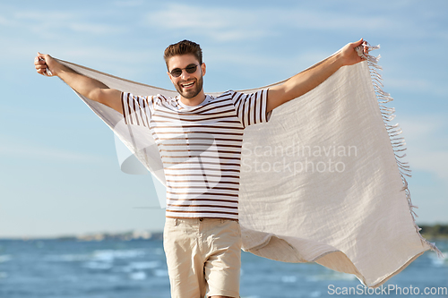 Image of smiling man in sunglasses with blanket on beach