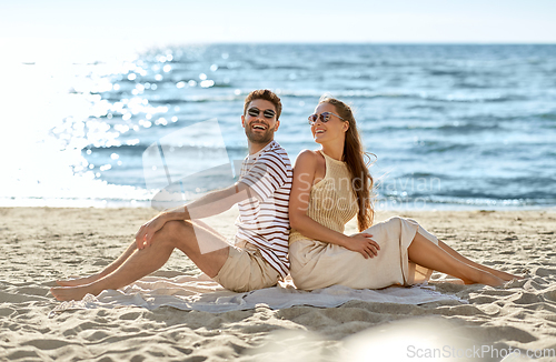 Image of happy couple sitting back to back on summer beach