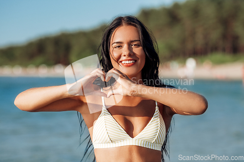 Image of smiling young woman in showing hand heart on beach