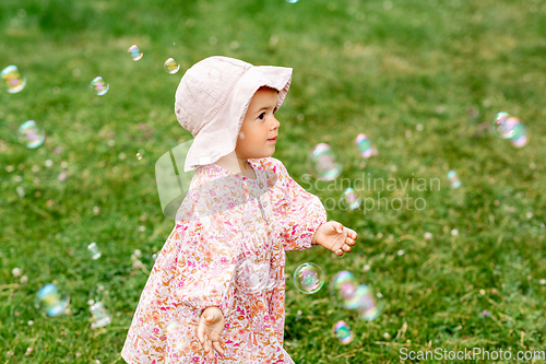 Image of happy baby girl playing with soap bubbles outdoors