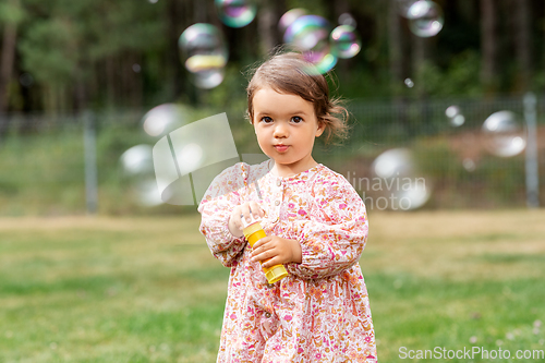 Image of happy baby girl blowing soap bubbles in summer
