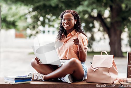 Image of african student girl in earphones with laptop