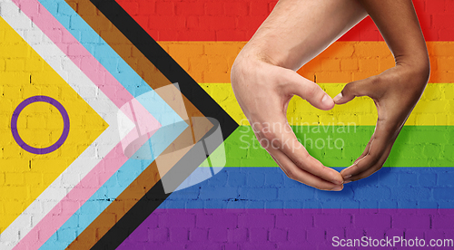 Image of couple showing hand heart over progress pride flag