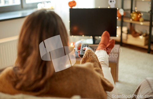 Image of young woman watching tv at home on halloween