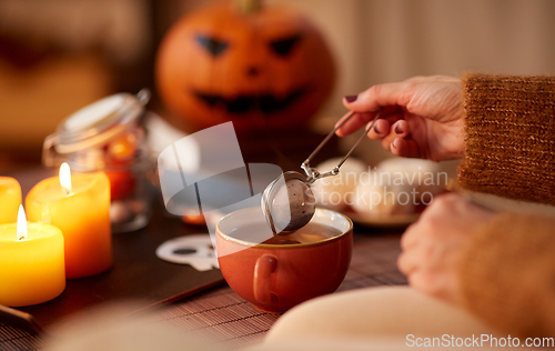 Image of woman's hand with tea infuser and mug on halloween