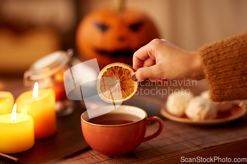 Image of hand adding dry orange to cup of tea on halloween