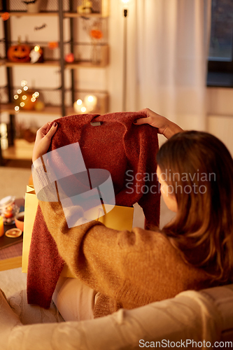 Image of woman taking cardigan from shopping bag at home