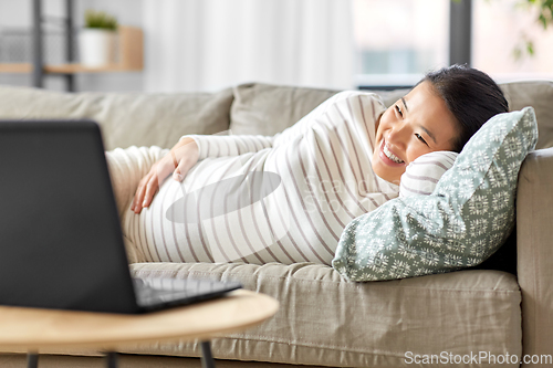 Image of happy pregnant asian woman with laptop at home