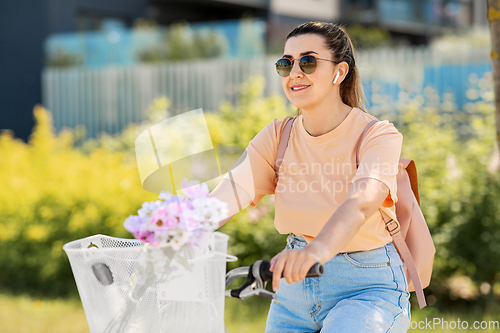 Image of happy woman with earphones riding bicycle in city