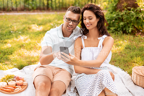 Image of happy couple with smartphone at picnic in park