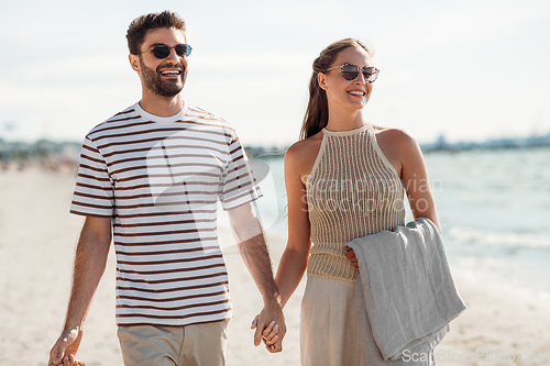 Image of happy couple with blanket walking along beach