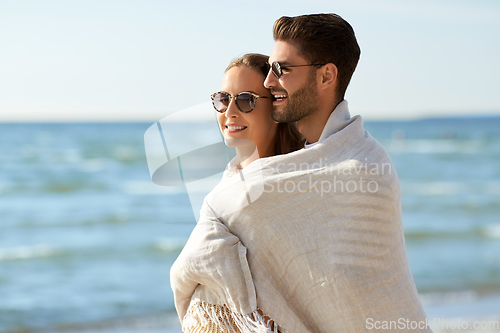 Image of happy couple covered with blanket hugging on beach