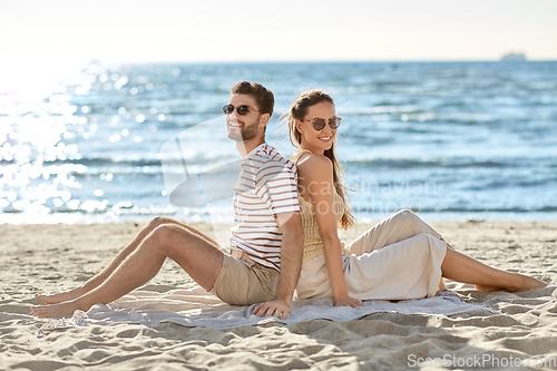 Image of happy couple sitting back to back on summer beach