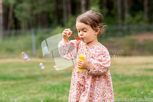 Image of happy baby girl blowing soap bubbles in summer