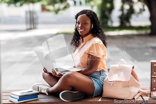Image of african student girl in earphones with laptop