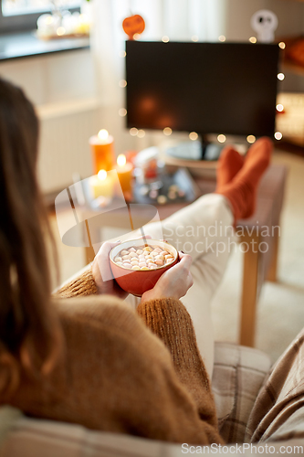 Image of woman watches tv and drinks cocoa on halloween