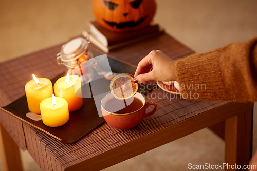 Image of hand adding dry orange to cup of tea on halloween