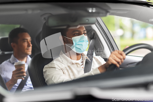 Image of male driver in mask driving car with passenger