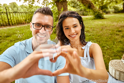 Image of happy couple making finger heart at summer park