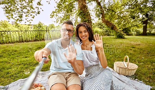 Image of happy couple taking selfie at picnic in park