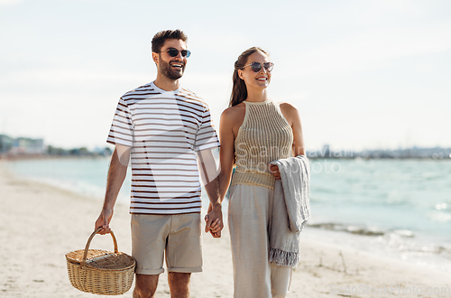 Image of happy couple with picnic basket walking on beach