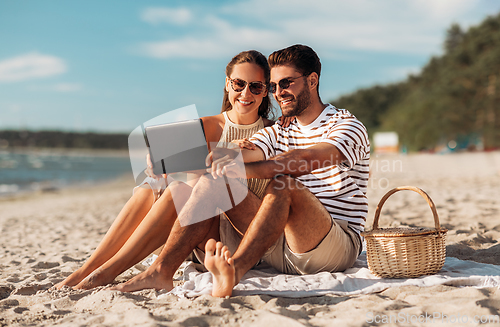 Image of happy couple with tablet pc at picnic on beach