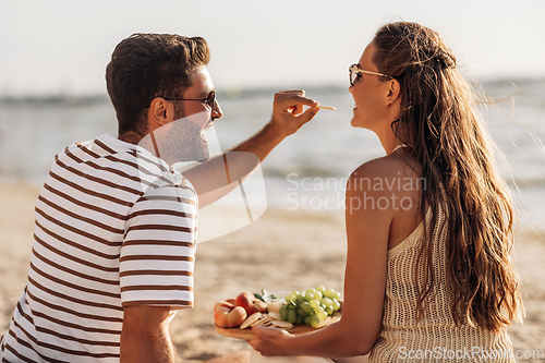 Image of happy couple with food having picnic on beach