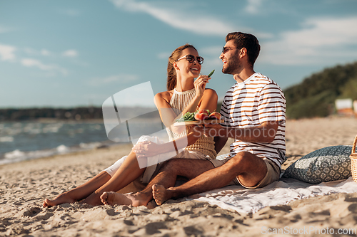 Image of happy couple with food having picnic on beach