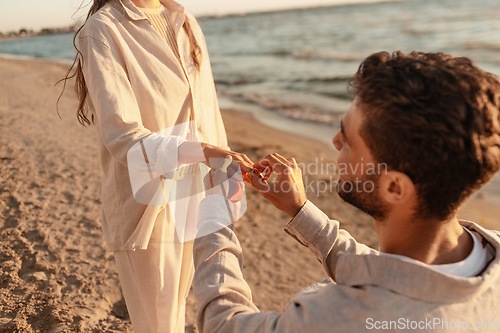 Image of man with ring making proposal to woman on beach
