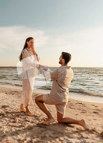 Image of man with ring making proposal to woman on beach