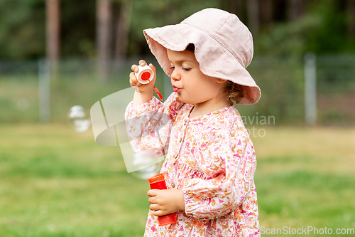 Image of happy baby girl blowing soap bubbles in summer