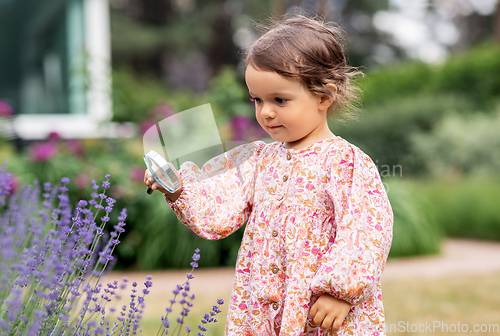 Image of baby girl with magnifier looking at garden flowers