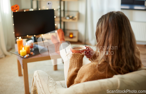 Image of woman watches tv and drinks cocoa on halloween