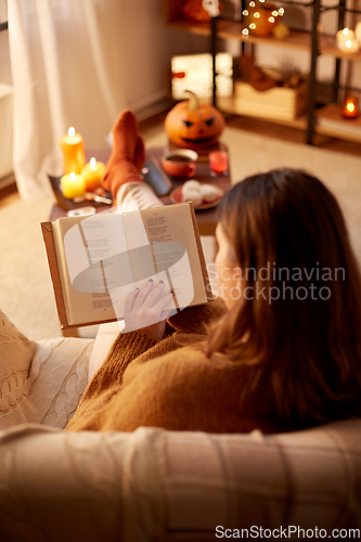 Image of young woman reading book at home on halloween