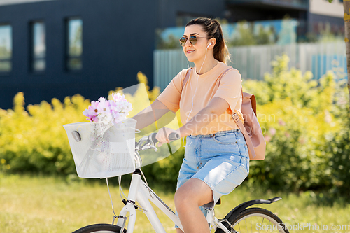 Image of happy woman with earphones riding bicycle in city