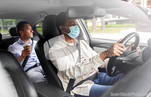 Image of male driver in mask driving car with passenger