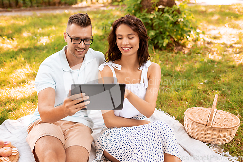 Image of happy couple with tablet pc at picnic in park