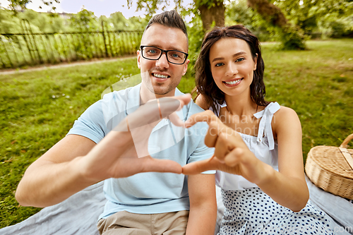 Image of happy couple making finger heart at summer park