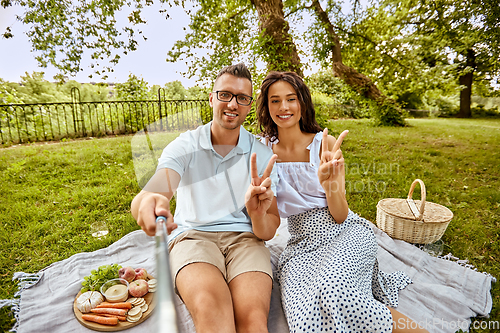 Image of happy couple taking selfie at picnic in park