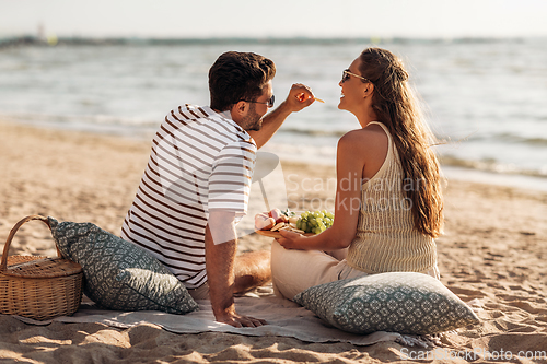 Image of happy couple with food having picnic on beach