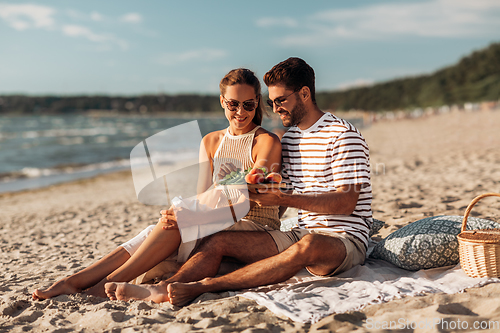 Image of happy couple with food having picnic on beach