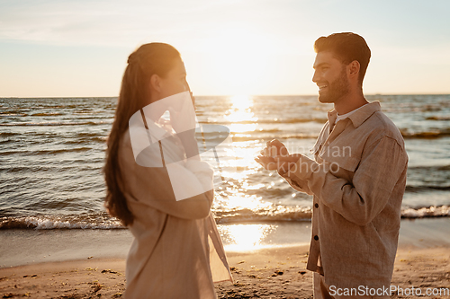 Image of man with ring making proposal to woman on beach