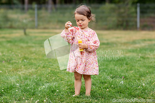 Image of happy baby girl blowing soap bubbles in summer